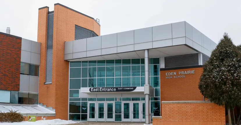 L'edificio scolastico moderno a più piani delle Eden Prairie Schools, con ampie vetrate e un ingresso caratteristico, è circondato da alberi.