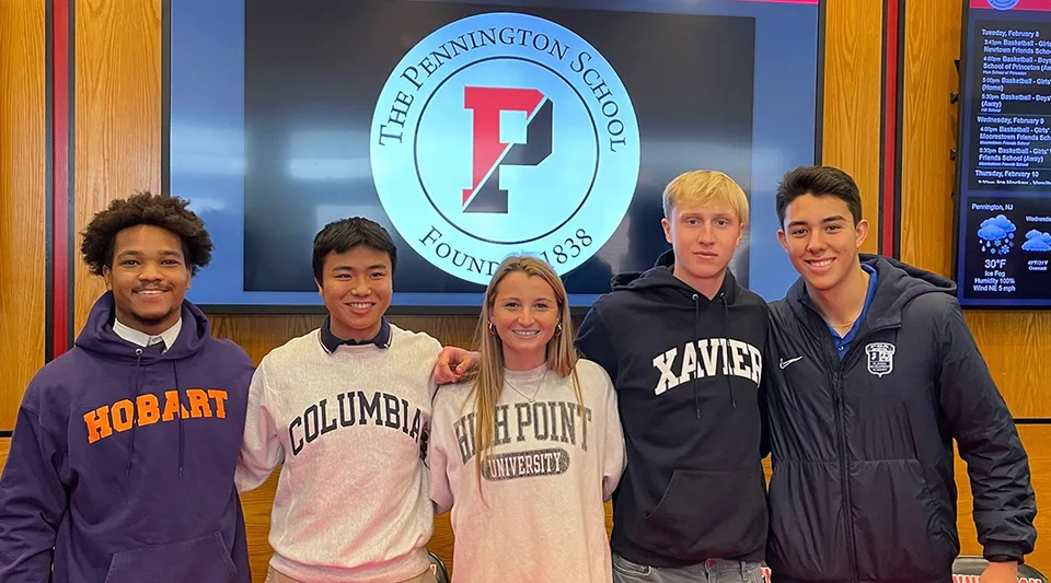 Un gruppo di cinque studenti sta davanti al logo della The Pennington School sulla parete.