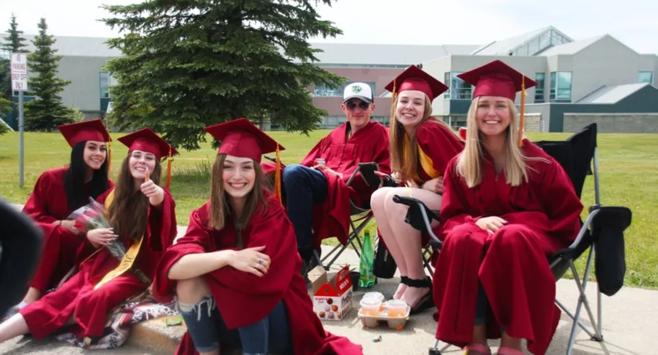 Un gruppo di studentesse della North Peace Secondary School indossa toge rosse da diploma e posa per una foto nel campus.
