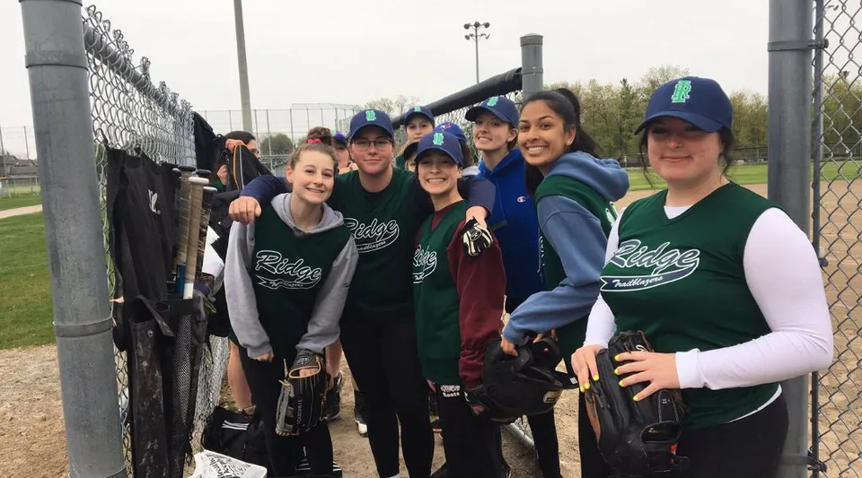 Un gruppo di studenti della Iroquois Ridge High School in posa insieme davanti a un campo sportivo recintato.