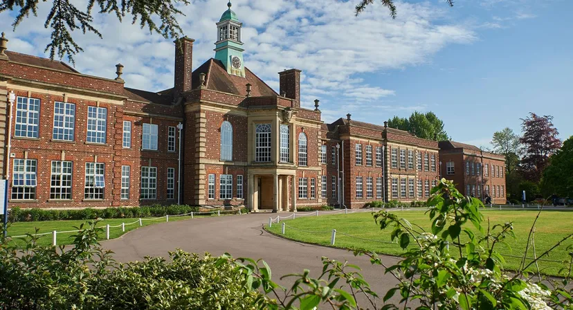 L'edificio storico in mattoni con un'alta torre nel campus della Headington School è circondato da un giardino ben curato.