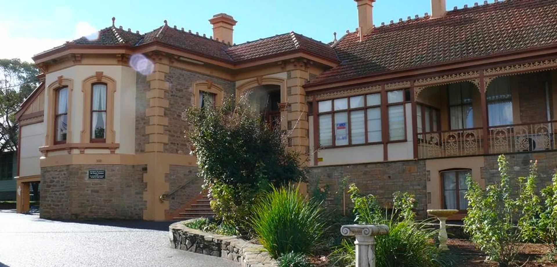 L'edificio principale storico della Kapunda High School con un giardino in primo piano sotto il cielo blu.