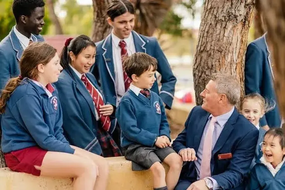 Studenti della John Septimus Roe Anglican Community School in divisa scolastica conversano all'aperto con un adulto in abito.