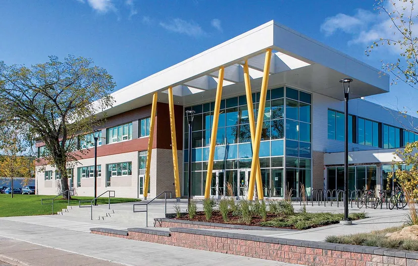 L'edificio moderno a più piani della Bowness High School, con elementi in vetro, bianchi e gialli, si trova in un ambiente circondato dal verde.