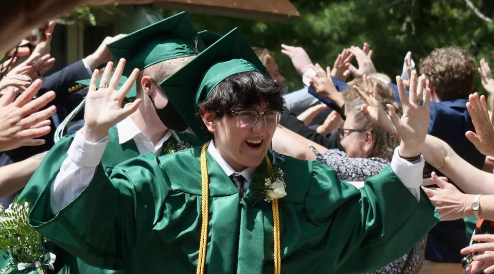 Diplomati della Leelanau School festeggiano con la toga verde e alzano le mani durante una cerimonia di diploma.
