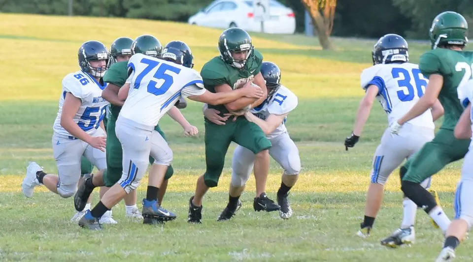 Giocatori della Metro East Lutheran High School durante una partita di football sul campo con alberi sullo sfondo.