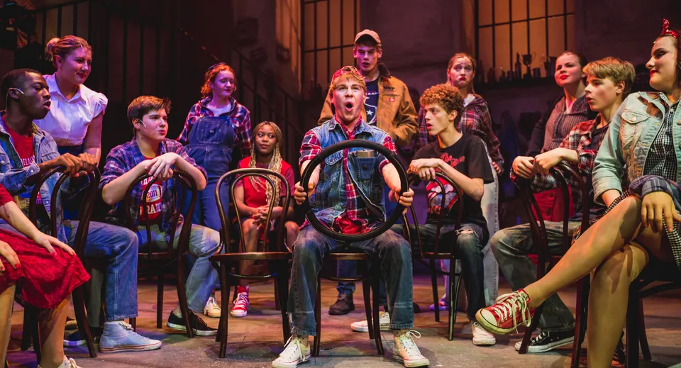 Un gruppo di studenti e studentesse della Uppingham School si riunisce nella scenografia di un teatro con illuminazione soffusa e un palco colorato sullo sfondo.