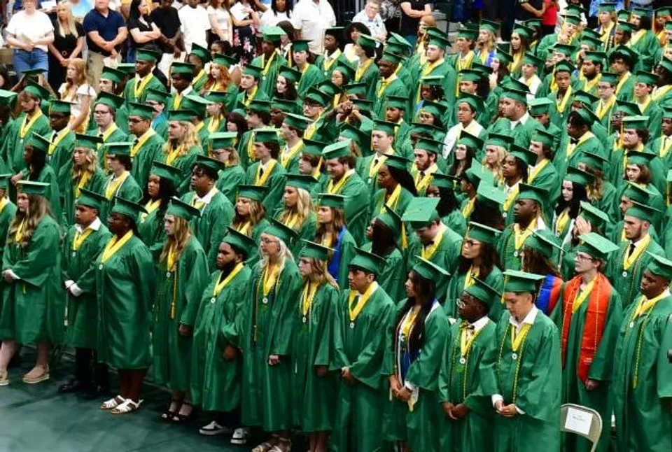 Un grande gruppo di diplomati e diplomate della Laurens Academy in toghe verdi e gialle posa insieme per una foto di gruppo.