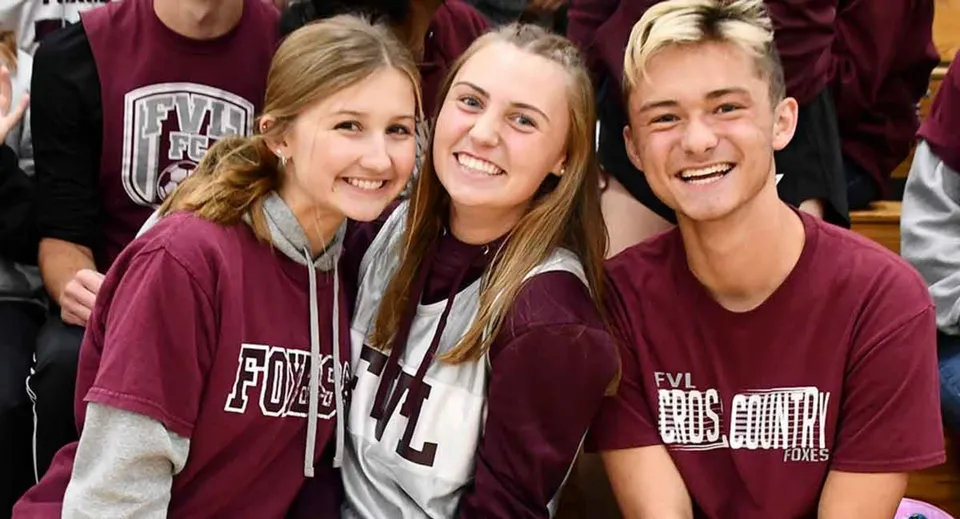 Tre studentesse della Northeastern Wisconsin Lutheran High School sorridono insieme in un ambiente scolastico.