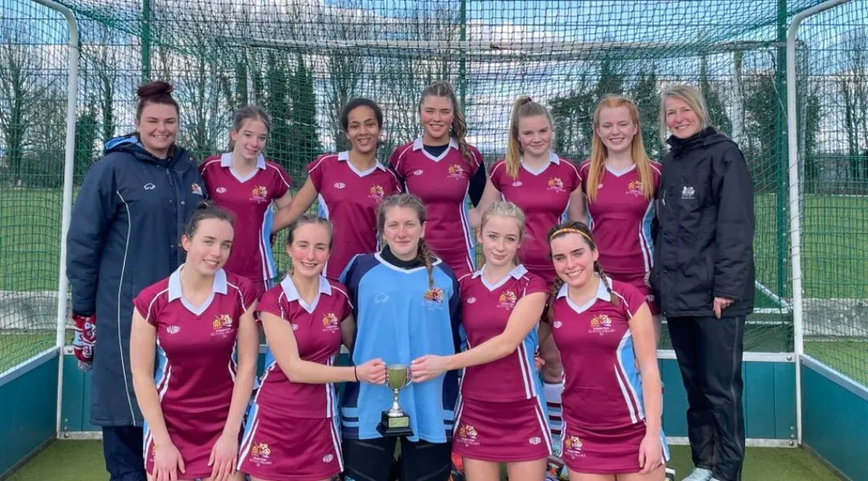 Un gruppo di giovani atlete in maglia rossa e blu posa su un campo sportivo nei terreni della Austin Friars School.