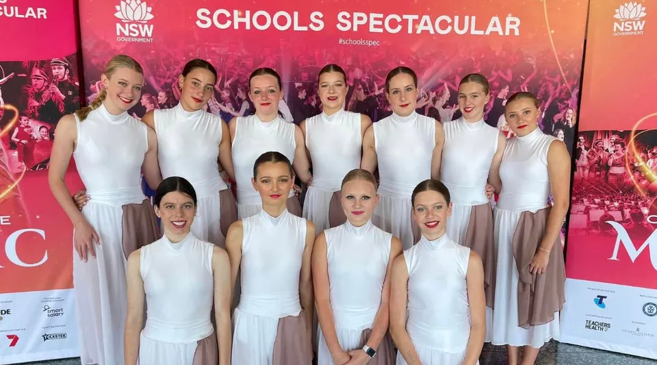Studentesse della Narrabeen Sports High School in posa su un palco davanti a un grande striscione rosso con la scritta Schools Spectacular.