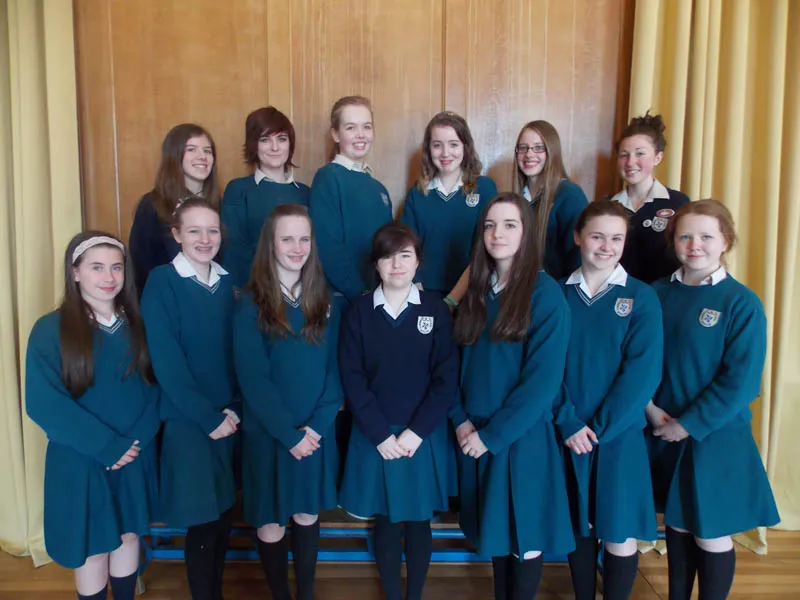 Un grupo de alumnas con uniforme escolar idéntico está delante de una pared revestida de madera en el campus del Dominican College Wicklow.