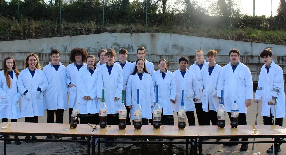 Un gruppo di studenti in camice bianco da laboratorio si trova nell'area del St. Michael's College davanti a un muro di cemento con alberi sullo sfondo.