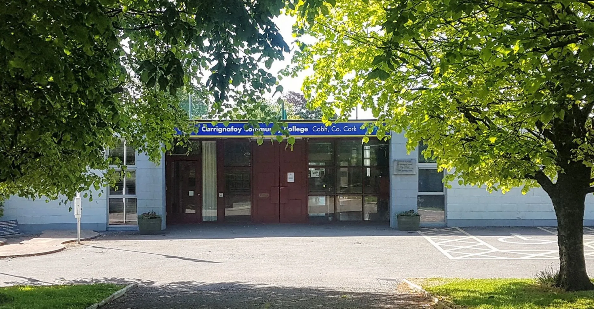 L'ingresso del Carrignafoy Community College con un edificio in mattoni e alberi verdi sullo sfondo.