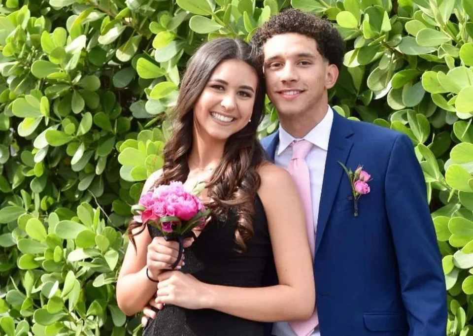 Una coppia sorride di fronte a uno sfondo verde con fiori nel campus della Lourdes Academy.