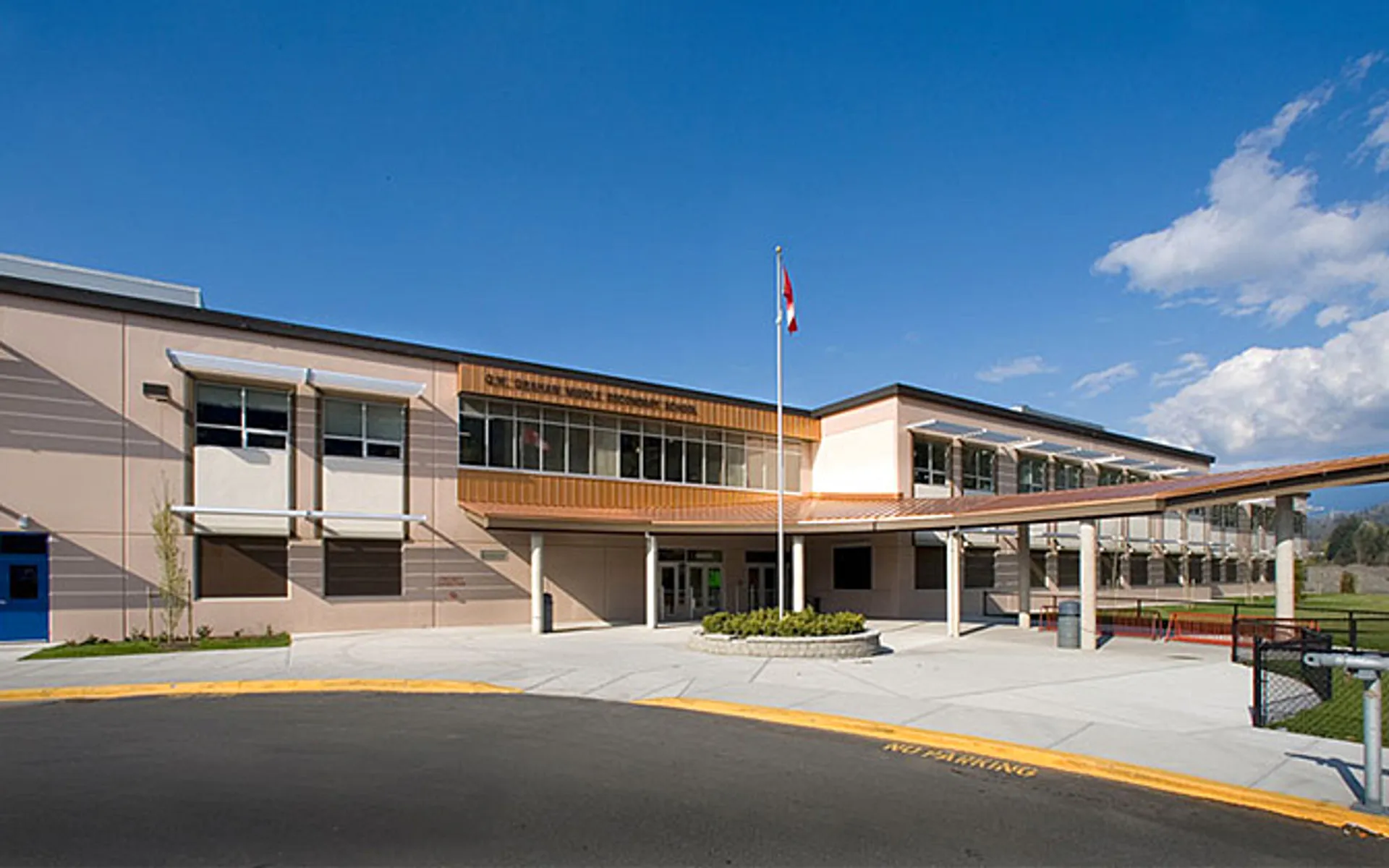 L'edificio a più piani della G.W. Graham Secondary School con un pennone e curati spazi esterni sotto un cielo blu.