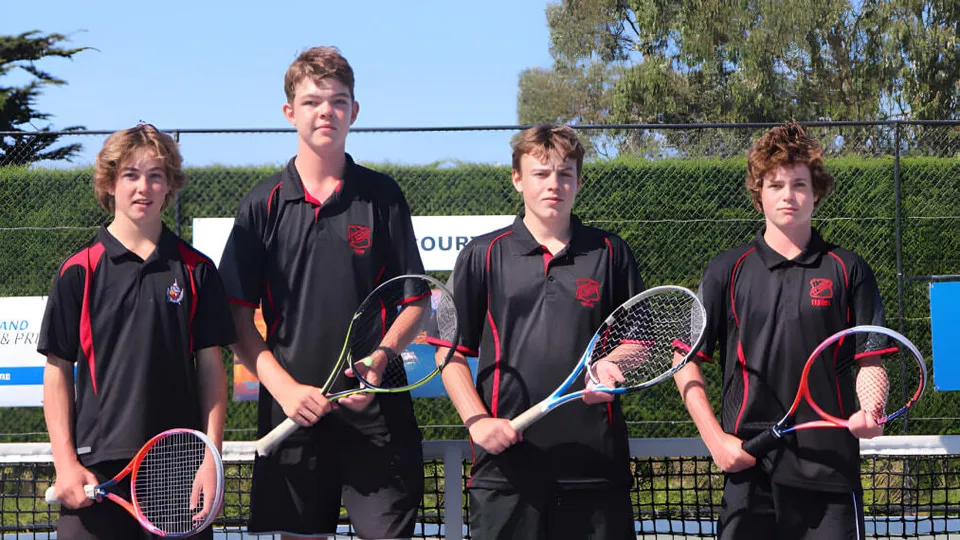 Quattro studenti del St. Bede's College sono in piedi sul campo da tennis con le racchette da tennis.