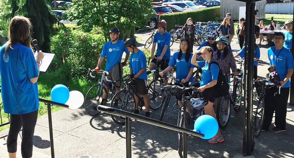 Un gruppo di studenti e studentesse della Windermere Secondary School è in piedi con le biciclette davanti a uno sfondo boscoso.