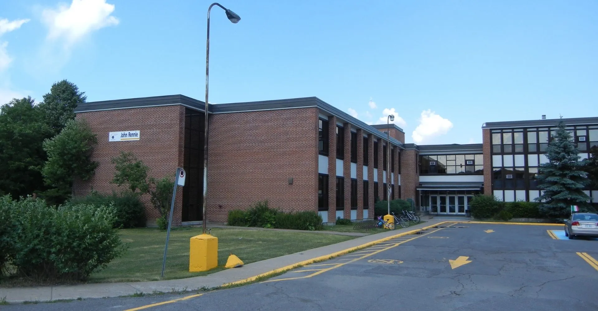 L'edificio in mattoni della John Rennie High School è circondato da aree verdi e si vede sotto un cielo azzurro e limpido.