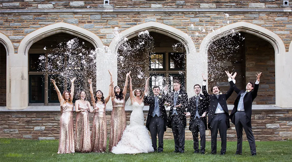 Gli studenti della St. Andrew's School festeggiano davanti a un edificio storico con finestre ad arco, lanciando confetti in aria.
