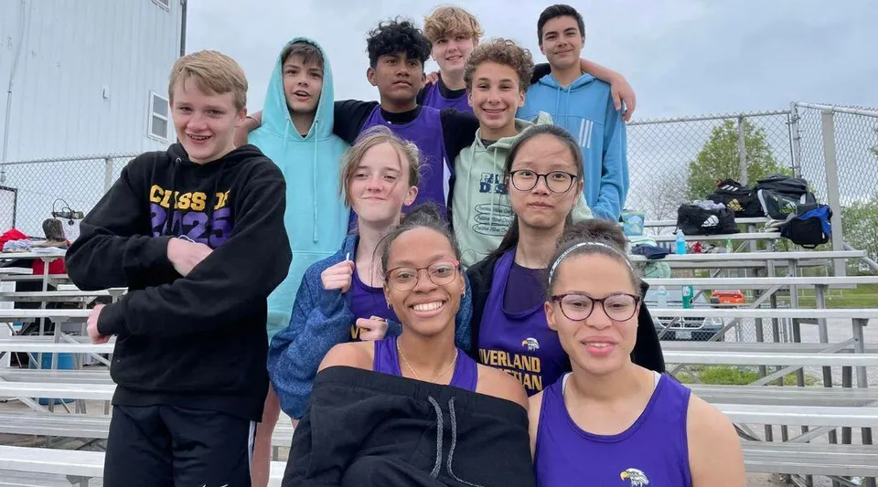 Un gruppo di studenti delle Overland Christian Schools sorride all'aperto davanti a una recinzione e a delle tribune.
