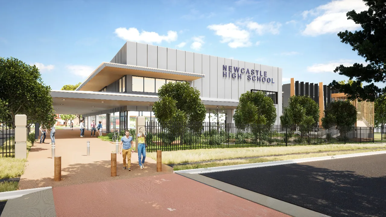 El moderno edificio escolar de dos plantas de Newcastle High School con entrada, árboles y un camino pavimentado en primer plano.