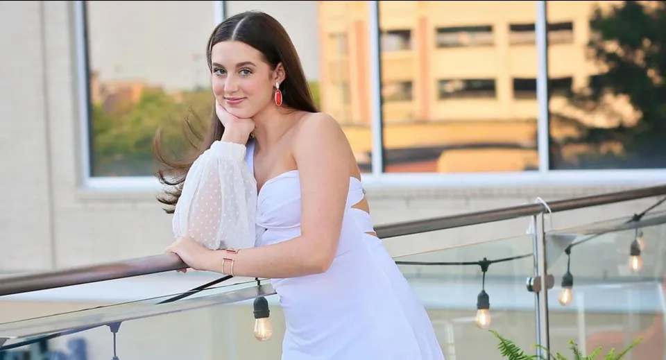 Una giovane donna in abito bianco si trova su un balcone con vista sulla città nel Blue Valley School District.