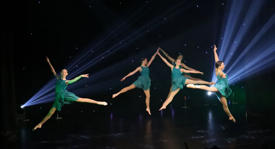 Un gruppo di ballerini esegue sul palco un'acrobazia aerea sincronizzata davanti a uno sfondo a forma di stella alla Cobham Hall School.