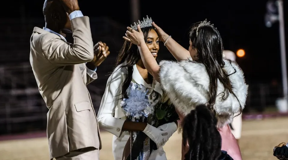 Una donna con corona e pelliccia a una festa alla Hamilton Christian Academy insieme ad altre due donne.