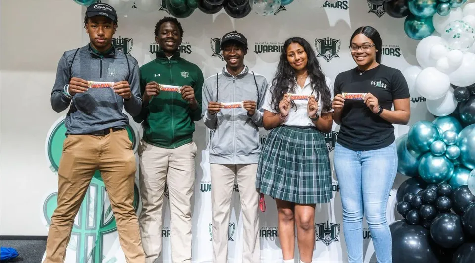 Studenti della Hamilton Christian Academy sono in piedi davanti a una parete con immagini sportive.