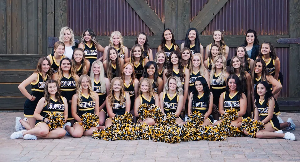 Un gruppo di cheerleader con i pompon posa insieme davanti a un edificio in legno nel campus del Chaffey Joint Union High School District.