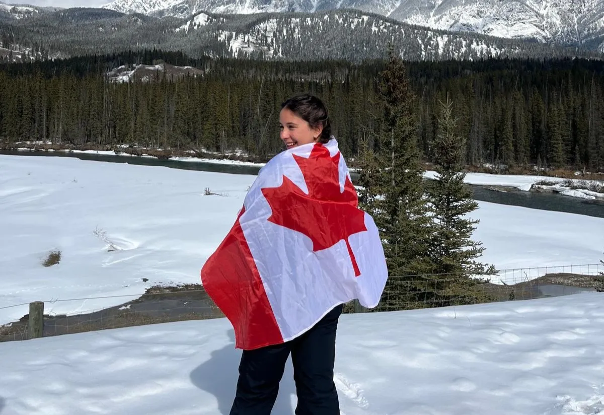 Ragazza avvolta nella bandiera canadese in un paesaggio innevato con abeti e montagne
