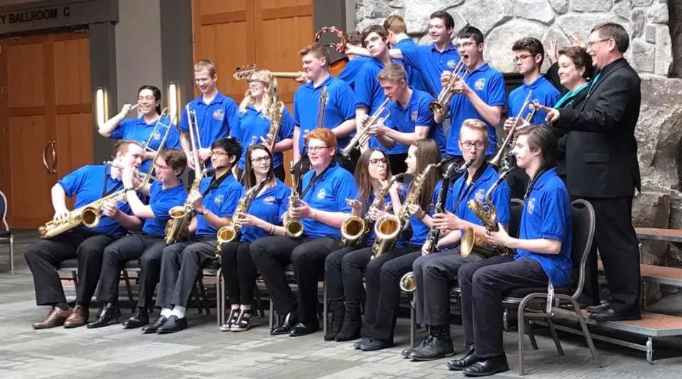 Studenti della John Maland High School in uniforme blu durante le prove d'orchestra davanti a un edificio in pietra.