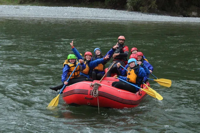 Grupo de jóvenes con casco y remo haciendo rafting en una balsa roja por el río