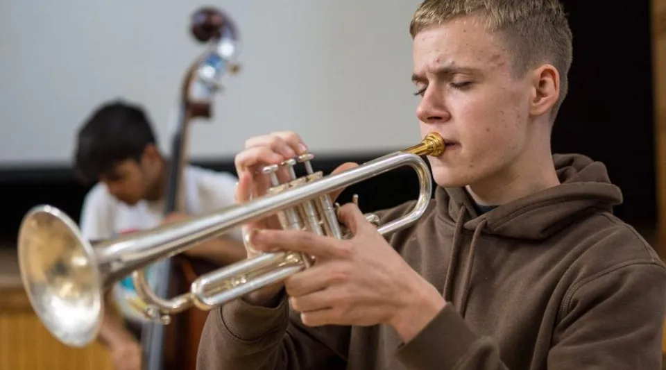 Un alunno della The Purcell School for Young Musicians suona la tromba mentre un altro studente suona il contrabbasso sullo sfondo.