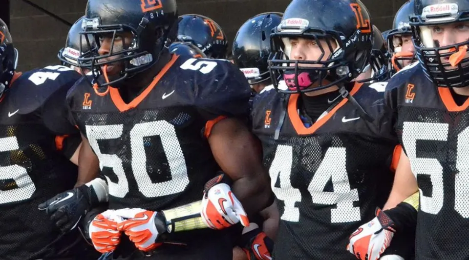 Un gruppo di giocatori di football della The Linsly School in divisa nera e arancione con il casco sul campo da gioco.