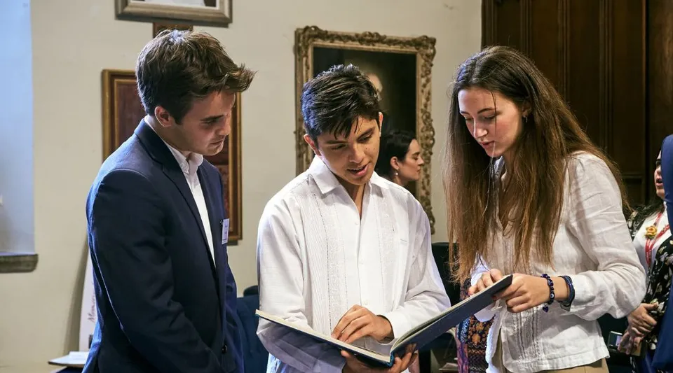 Due studenti e una studentessa del UWC Atlantic College esaminano insieme un documento davanti ad alcune opere d'arte.