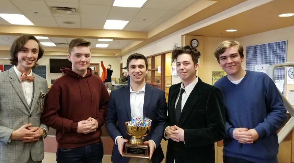Cinque studenti della North Grenville District High School mettono in posa insieme con un trofeo in un corridoio con armadietti.