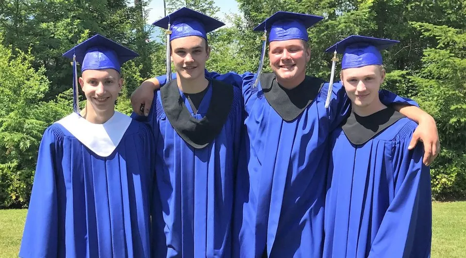 Quattro studenti in toga da diploma blu si trovano in un'area alberata nel campus della Alberni District Secondary School.