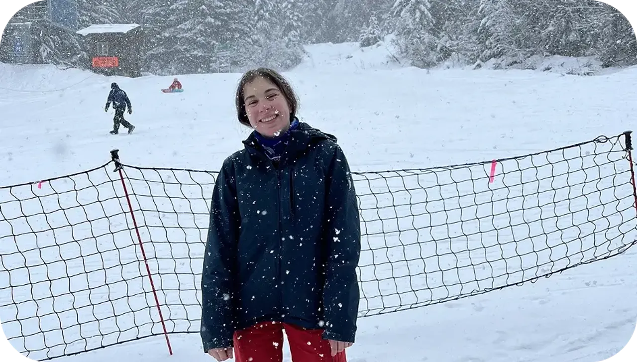 Ragazza sorridente con giacca invernale sotto la neve su una pista da sci