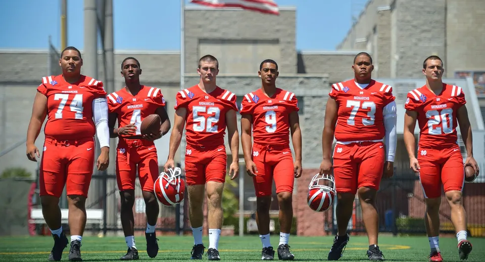 Un gruppo di calciatrici e calciatori della Washington Academy in maglia rossa si trova sul campo da gioco davanti a un edificio con la bandiera americana.