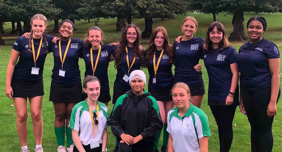 Un gruppo di studentesse della Wychwood School è insieme all'aperto su un prato davanti ad alcuni alberi in divisa sportiva.