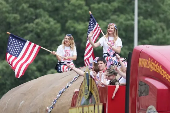 Jóvenes ondean banderas de Estados Unidos sobre una carroza en un desfile al aire libre