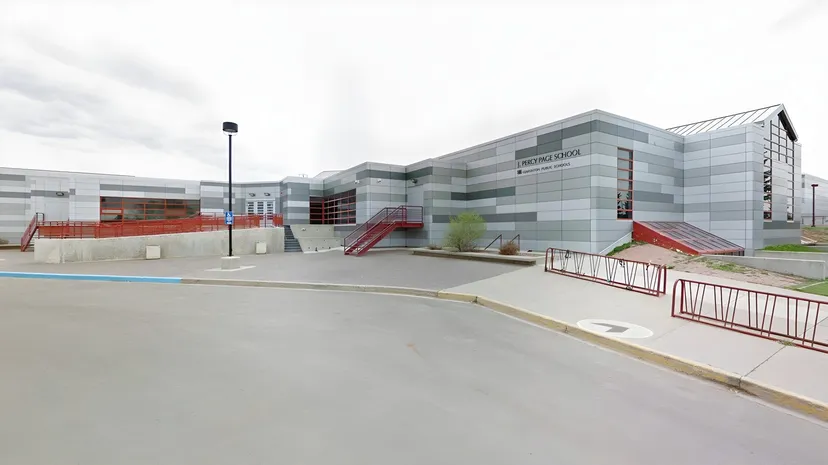 L'edificio moderno a più piani della J. Percy Page High School con facciata in vetro e metallo è circondato da un'area pavimentata con transenne rosse.