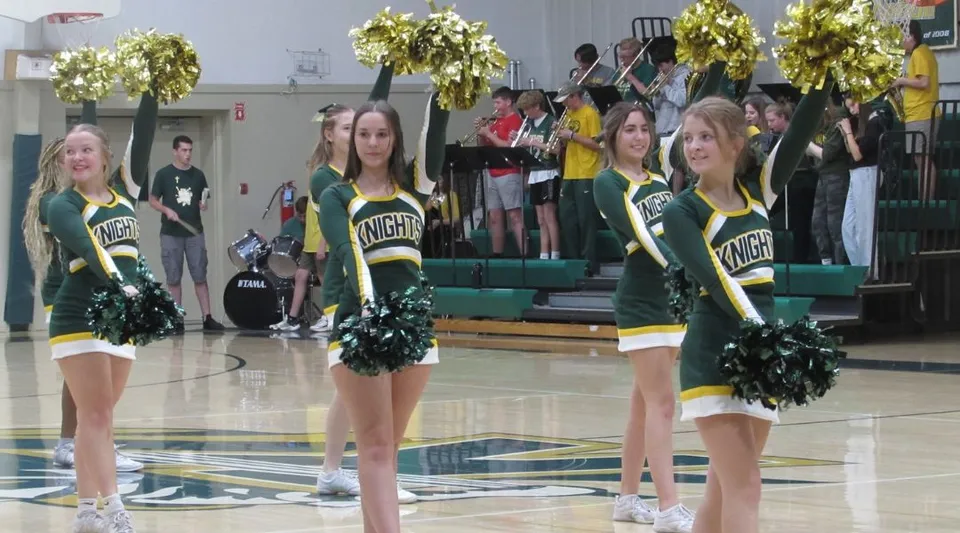 Cheerleader della Metro East Lutheran High School in divisa verde e gialla sul campo da basket davanti al pubblico.