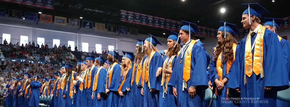 Un gruppo di diplomati in tocco e toga blu e oro sul palco della Chelsea High School durante la cerimonia di diploma.