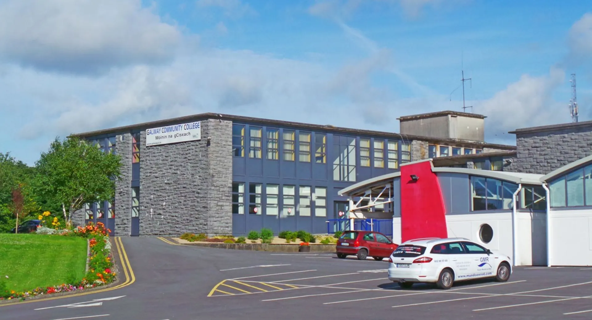 L'edificio del Galway Community College con facciata in pietra e vetro e un parcheggio in primo piano.