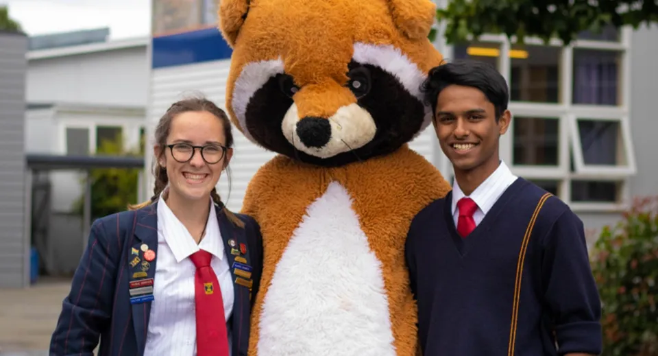 Due persone in abbigliamento formale davanti a una grande scultura a forma di animale nel campus della Riccarton High School.