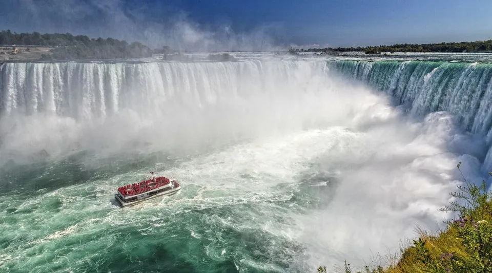 Una barca con passeggeri naviga davanti a una cascata vicino alla Georgetown District High School.