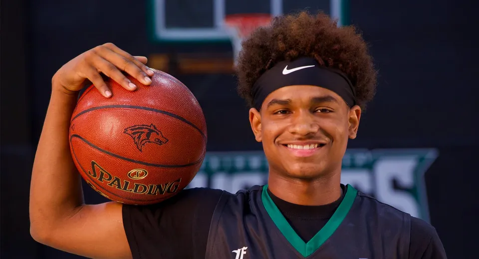 Uno studente della Fairmont Prep Academy con capelli ricci e fascia Nike tiene in mano un pallone da basket davanti al campo da basket.